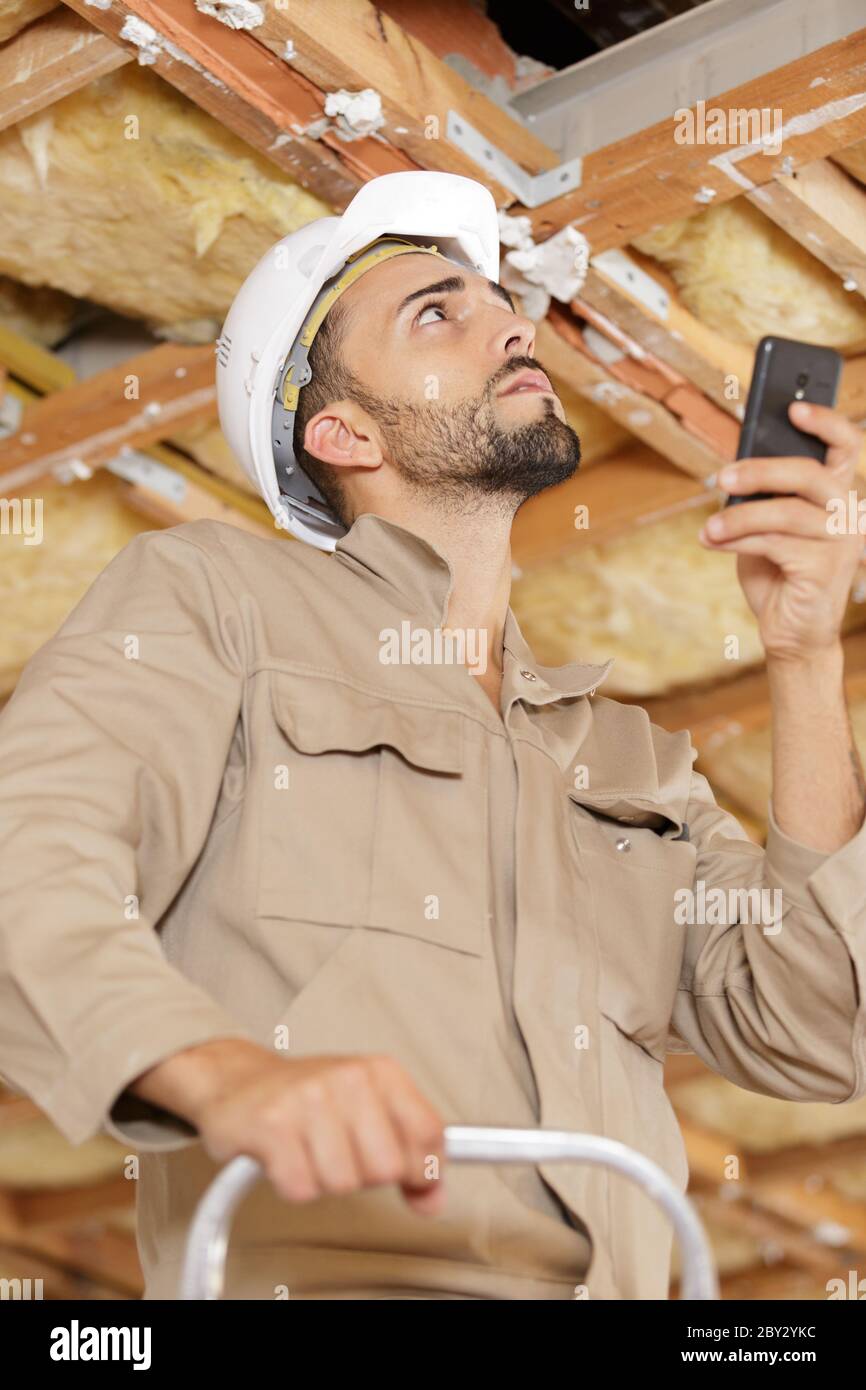 builder stood on stepladder holding smartphone Stock Photo
