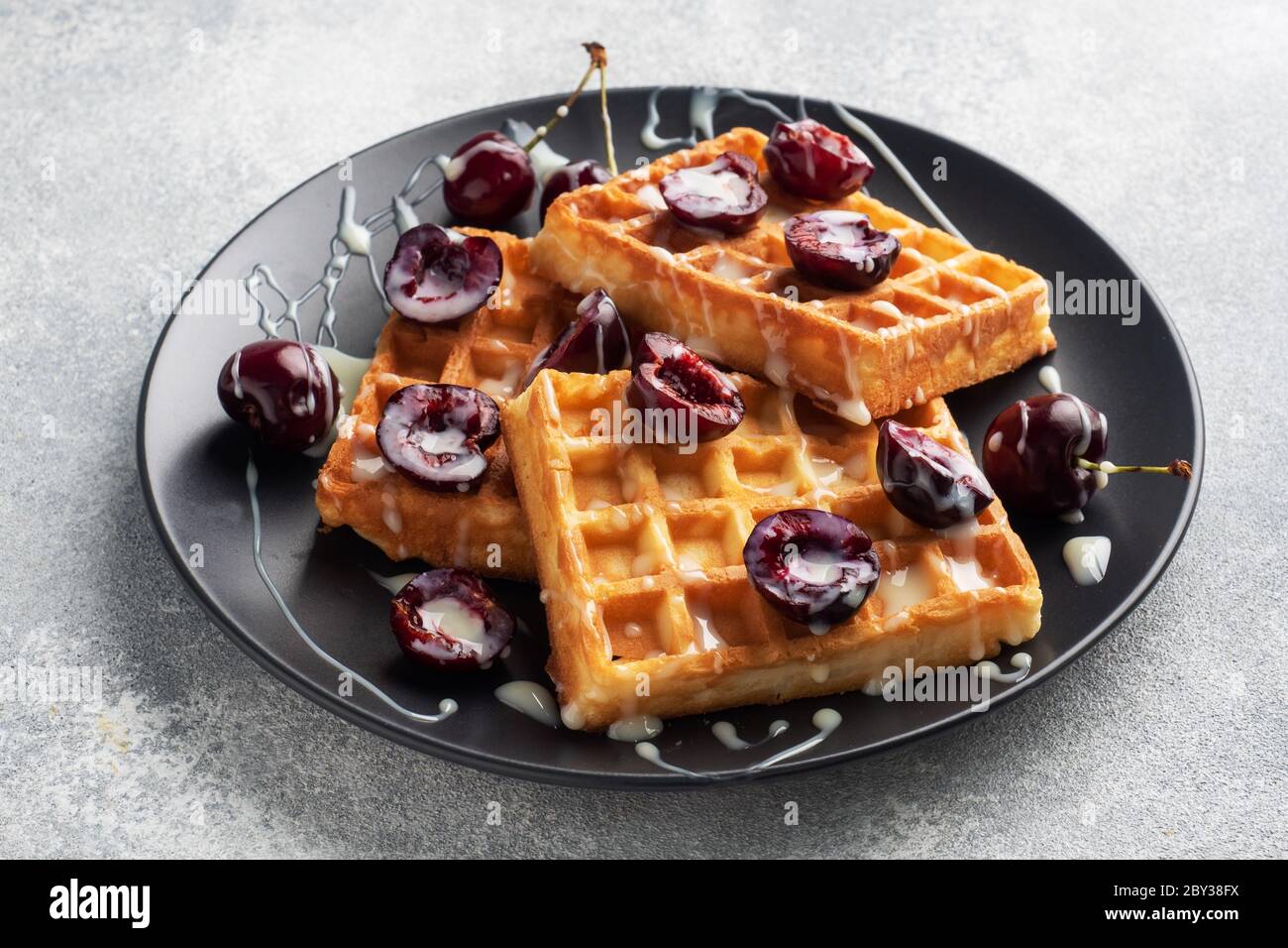 Belgian fluted waffles with fresh cherries and cream on a plate. Soft homemade waffles, sweet dessert with cherries Stock Photo