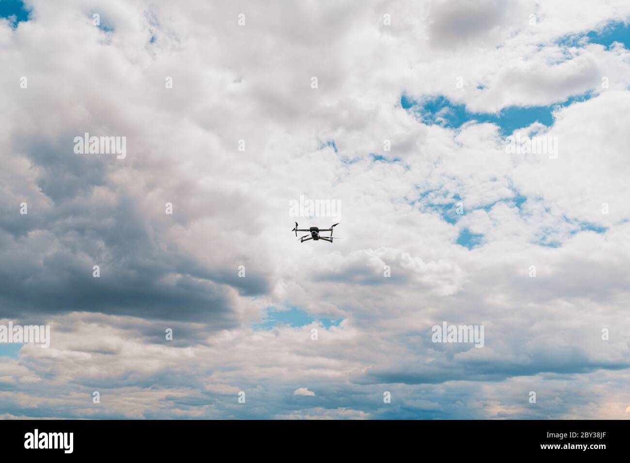 Drone flying overhead in cloudy blue sky Stock Photo