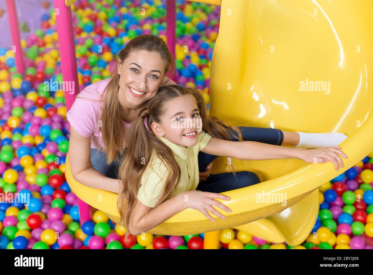 Cheerful girl with her mom sitting on slide at indoor children playground Stock Photo
