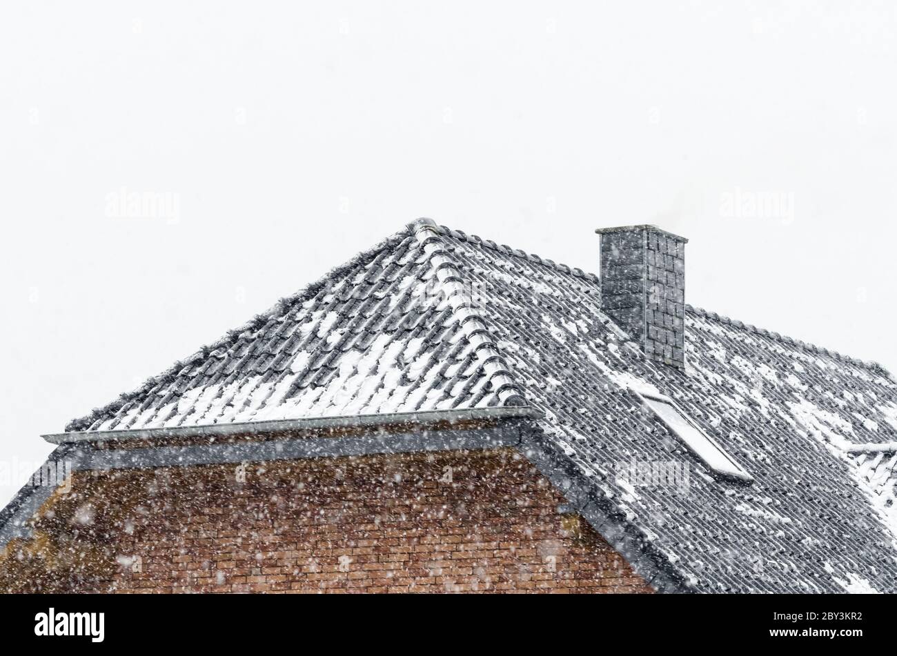 Snow covered roof and chimney of a house during heavy snowfall in wintertime in Germany Stock Photo