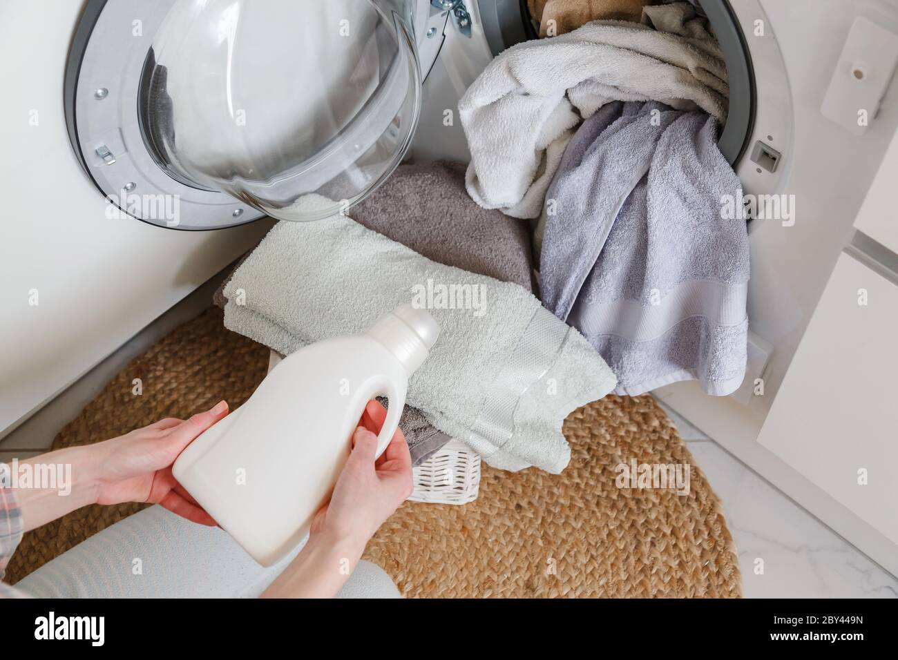 Woman holds bottle with liquid laundry detergent before washing clothes