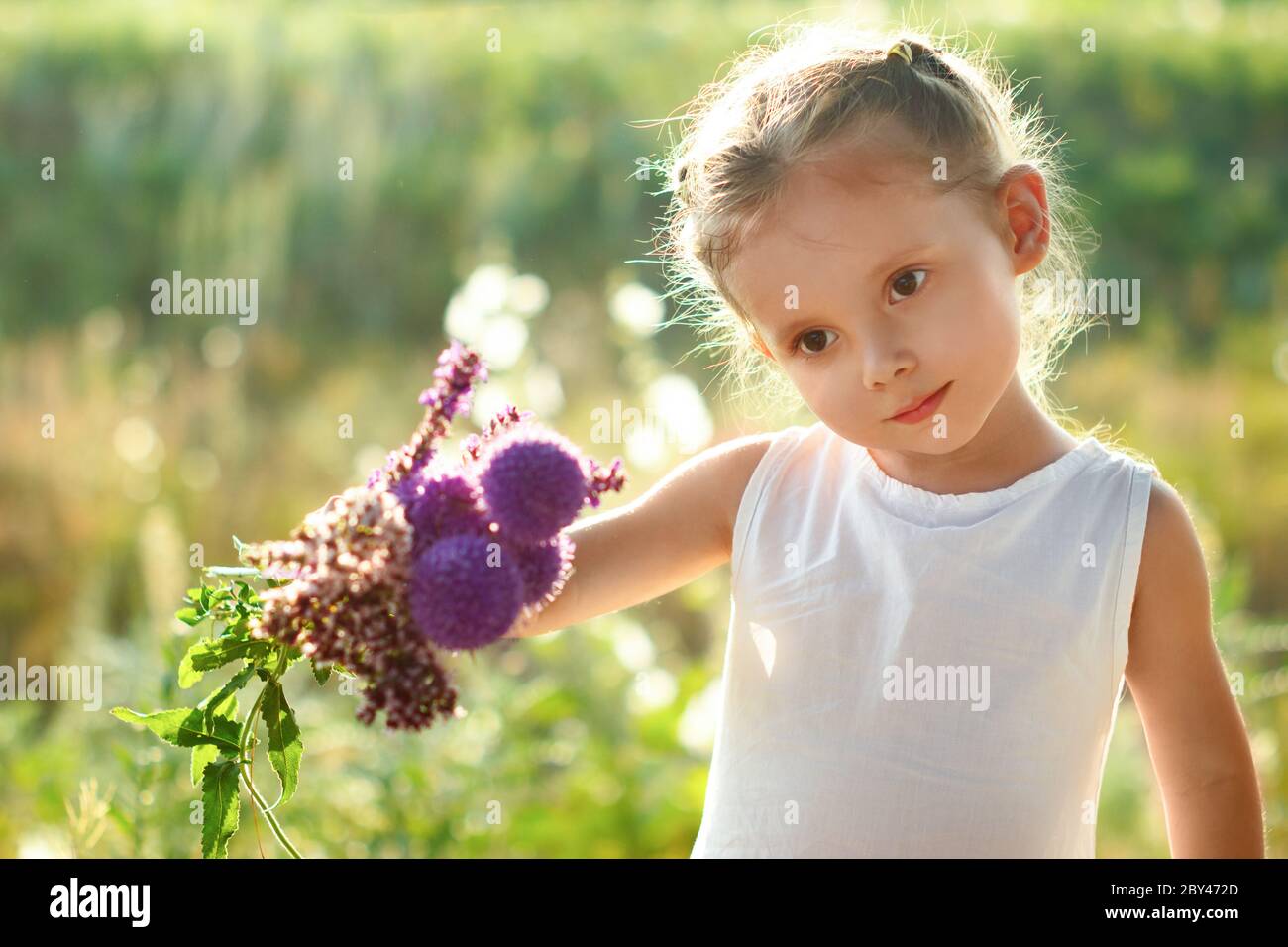 Little cute girl in white dress with a summer bouquet of wildflowers in ...