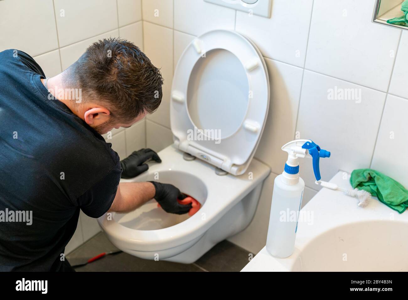 A professional cleaner cleans a ceramic toilet very thoroughly in a