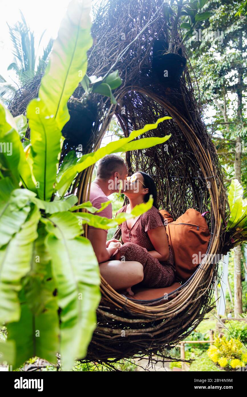 A tourist couple sitting on a large bird nest on a tree at Bali island