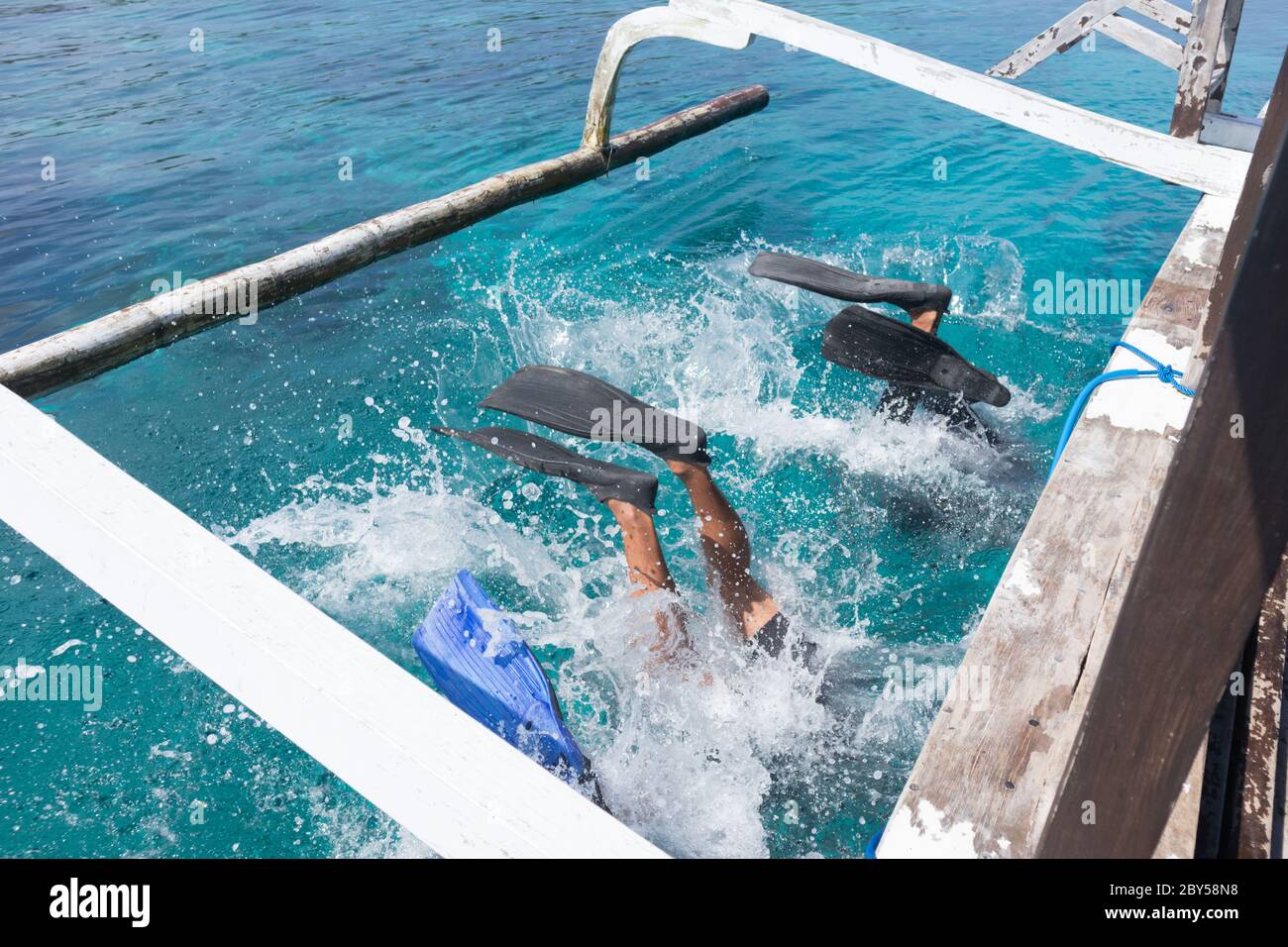 Scuba divers doing back flip into blue transparent sea from a boat's board. There are several ways to get off the boat when diving. One of them is by Stock Photo