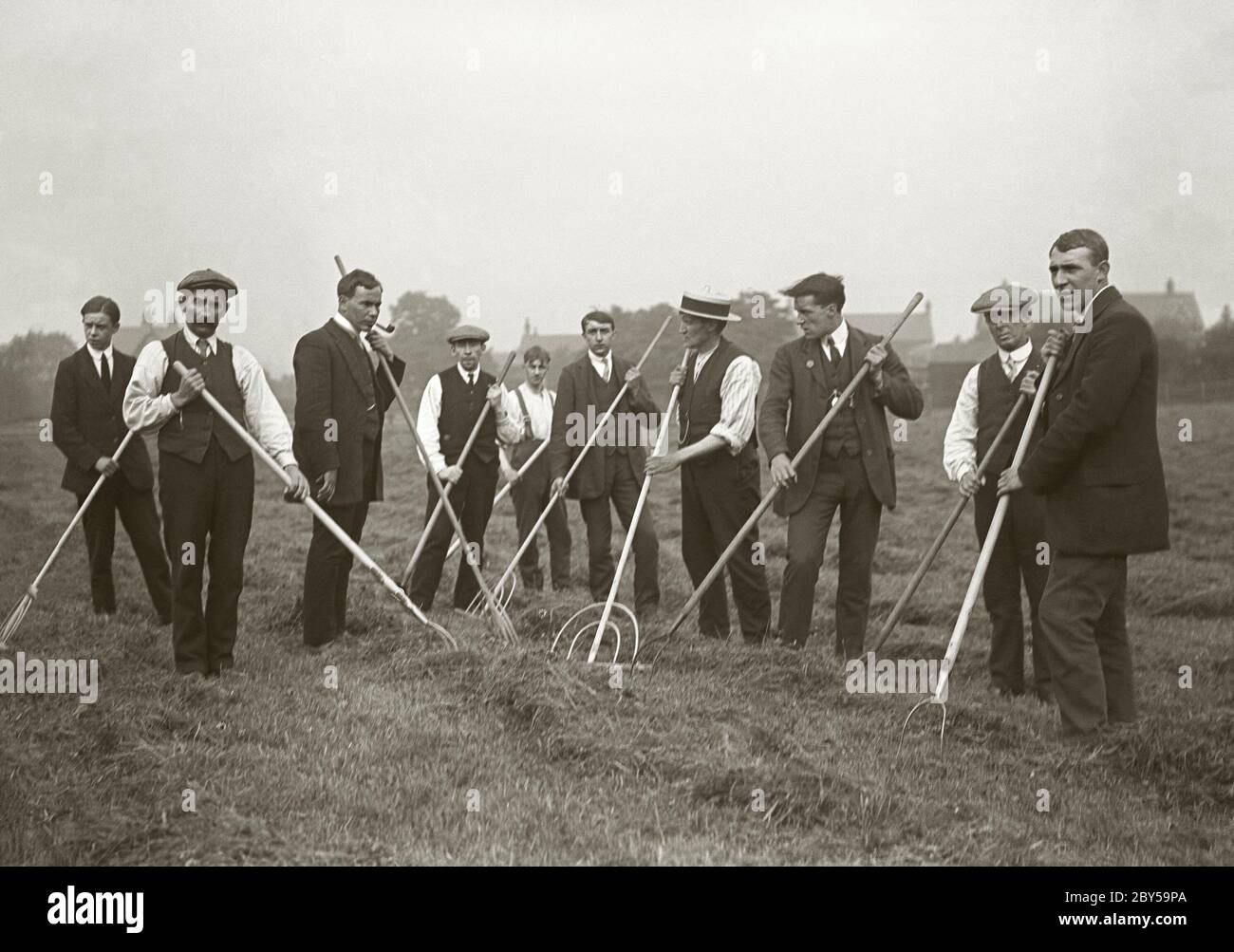 Ten farm workers with their rakes in a grass meadow begin to rake up the cut grass for hay making, UK c. 1900. They are smartly dressed for the task with most wearing ties and some suits. Stock Photo