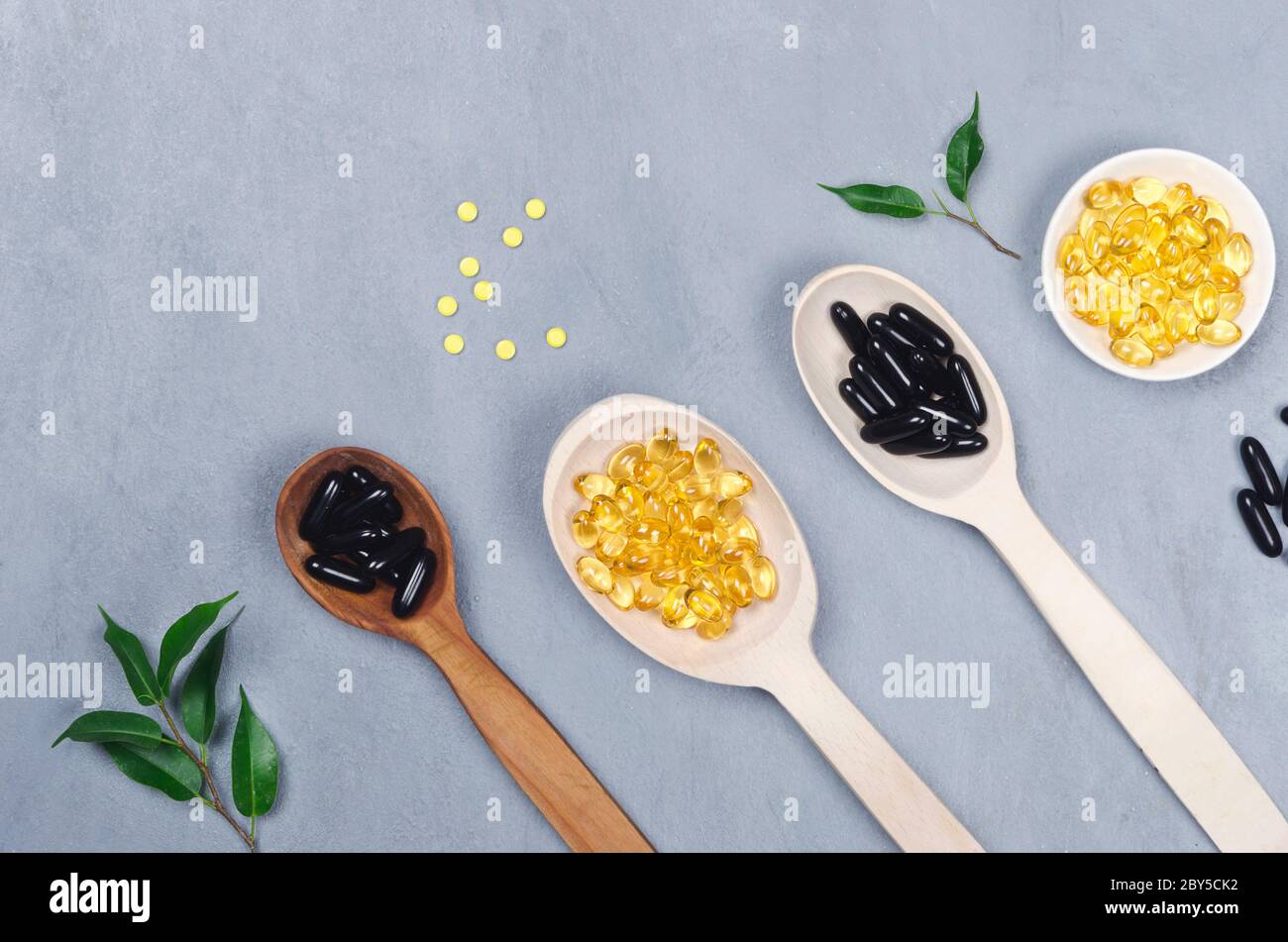 Black and yellow pills on wooden spoons on gray background Stock Photo