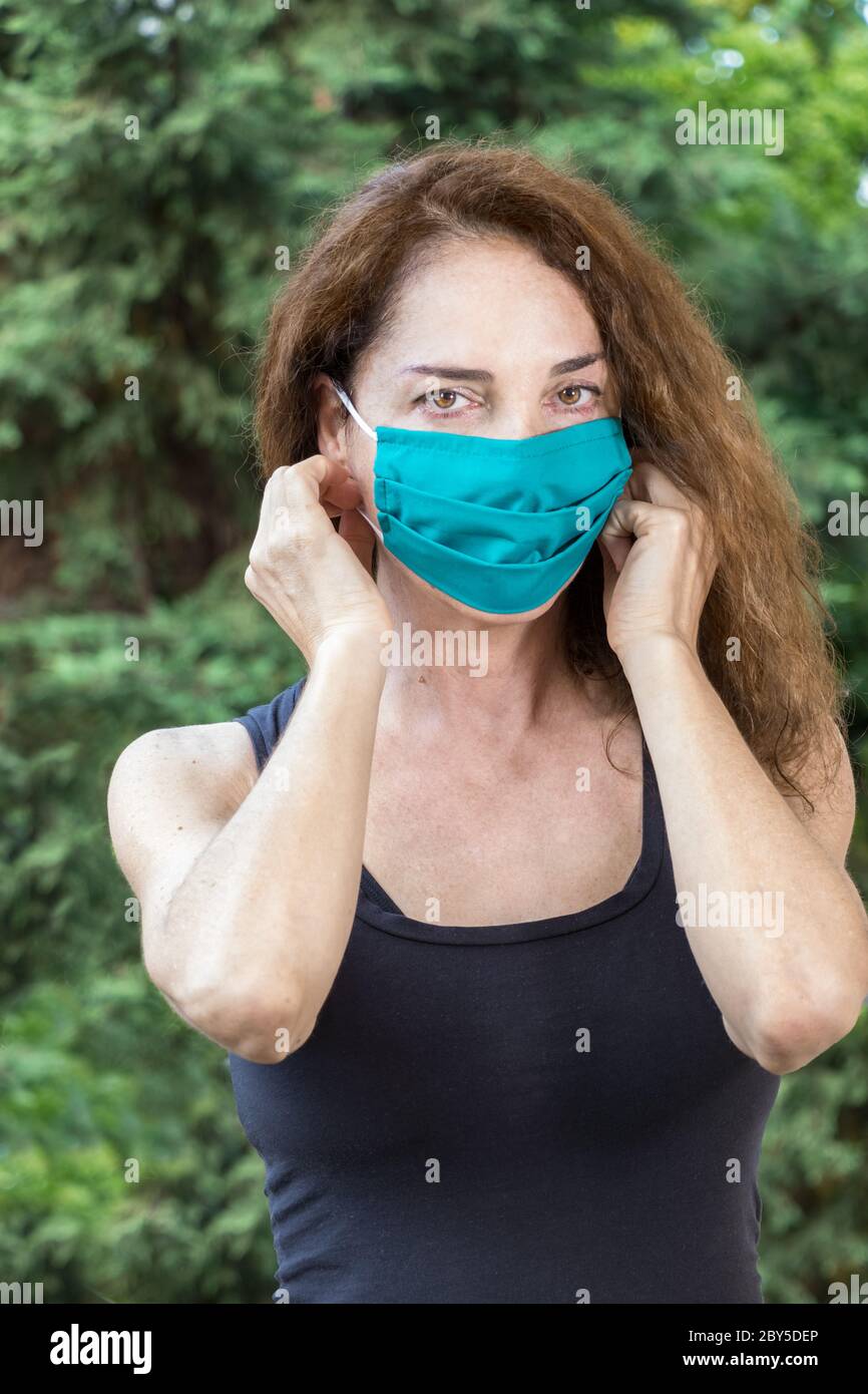 A fit woman putting on a protective mask in summer looking camera, outdoors Stock Photo