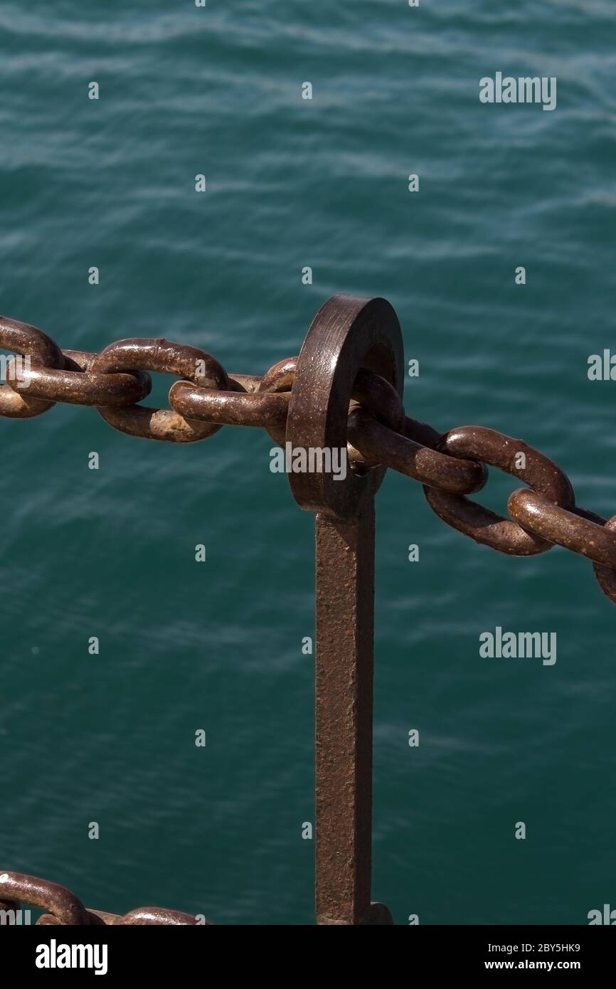 rusty iron chains handrail before turquoise water Stock Photo