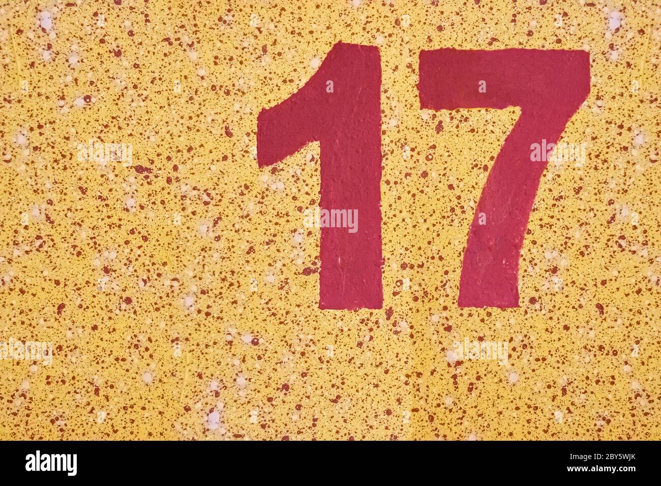 Number seventeen red color painted on a yellow wall with splashes. Stock Photo