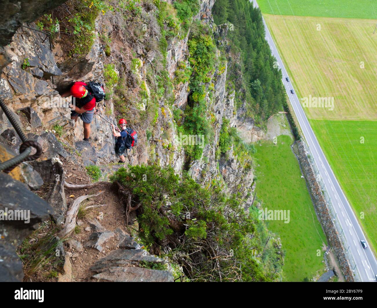 Via ferrata climbers holds steel cable high above road, Reinhard Schiestl Klettersteig, Austria Stock Photo