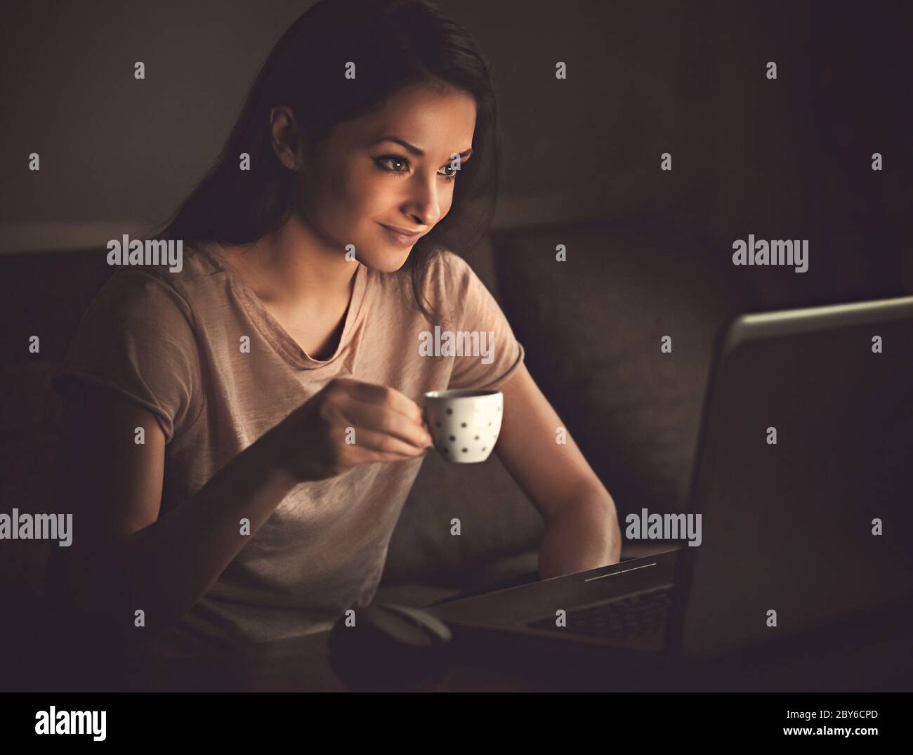 Smiling thinking beautiful woman looking on computer monitor drinking