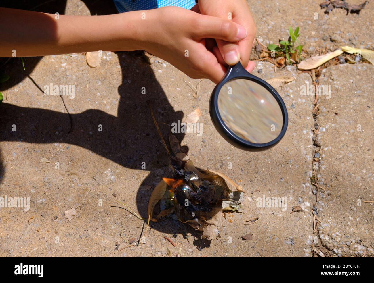 Hands of a young boy using a magnifying glass to start a fire. View of