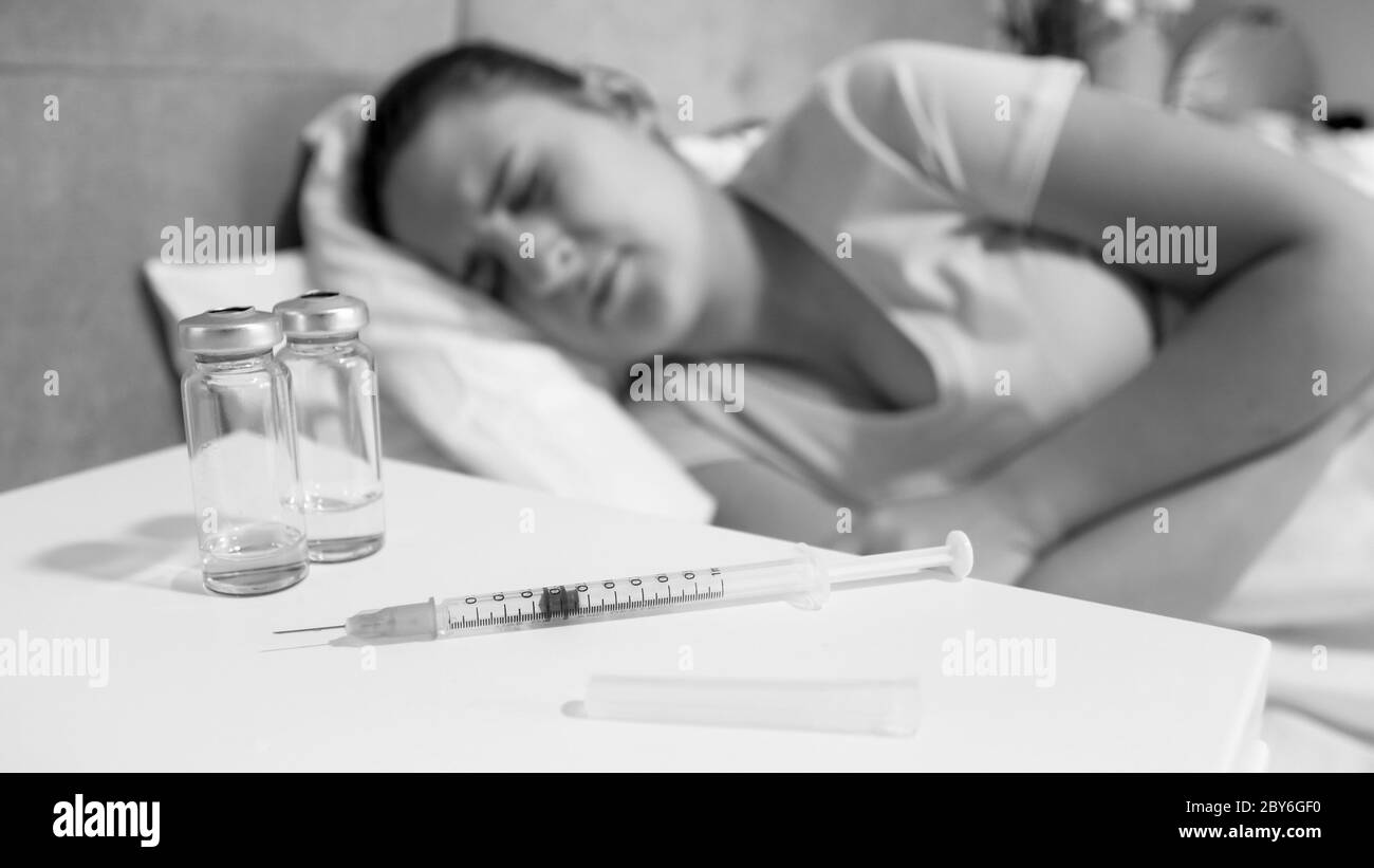 Black and white image of sick woman with drug addiction lying in bed and looking on syringe Stock Photo