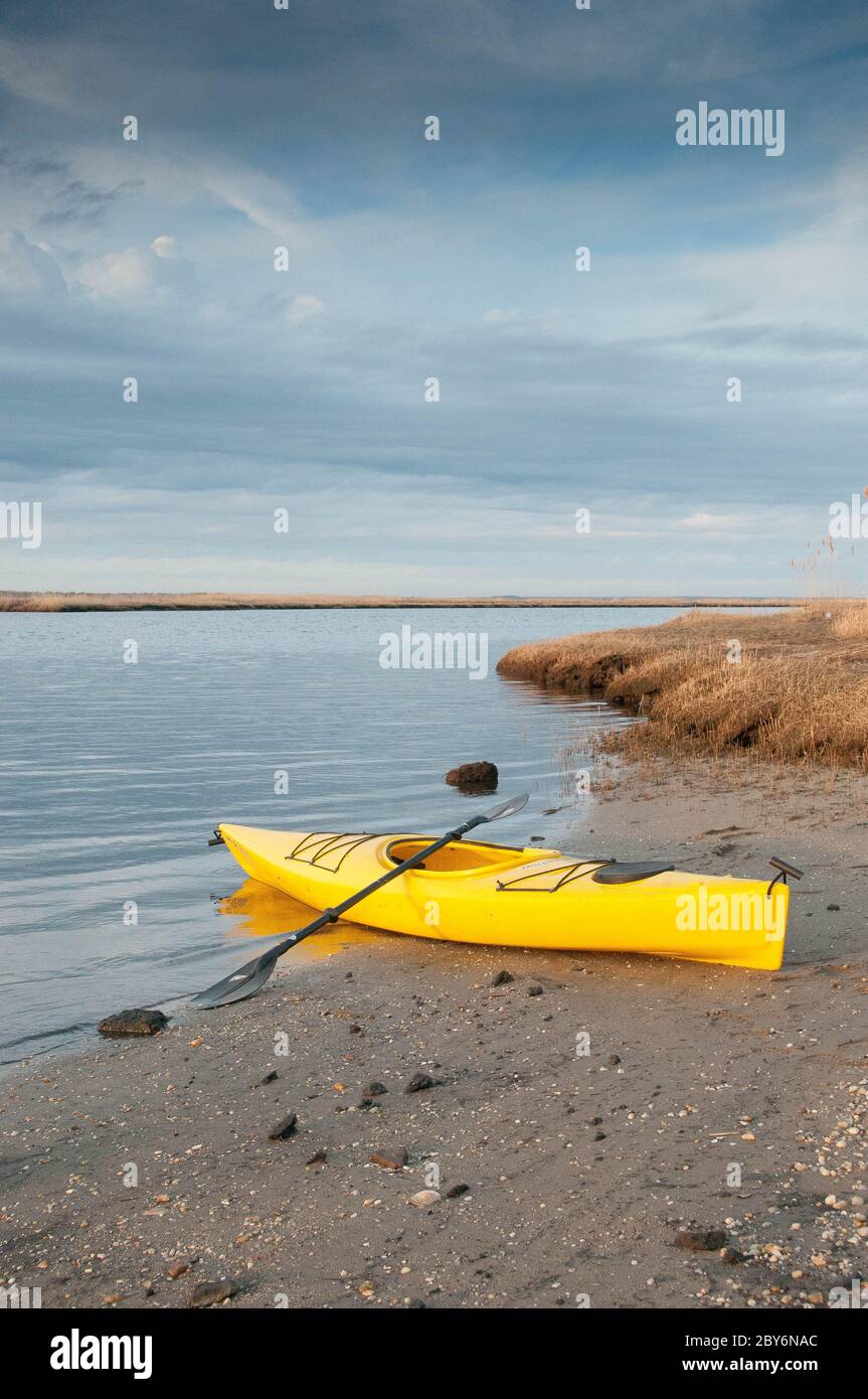 A bright yellow kayak is poised for launch on the beach along the river Stock Photo