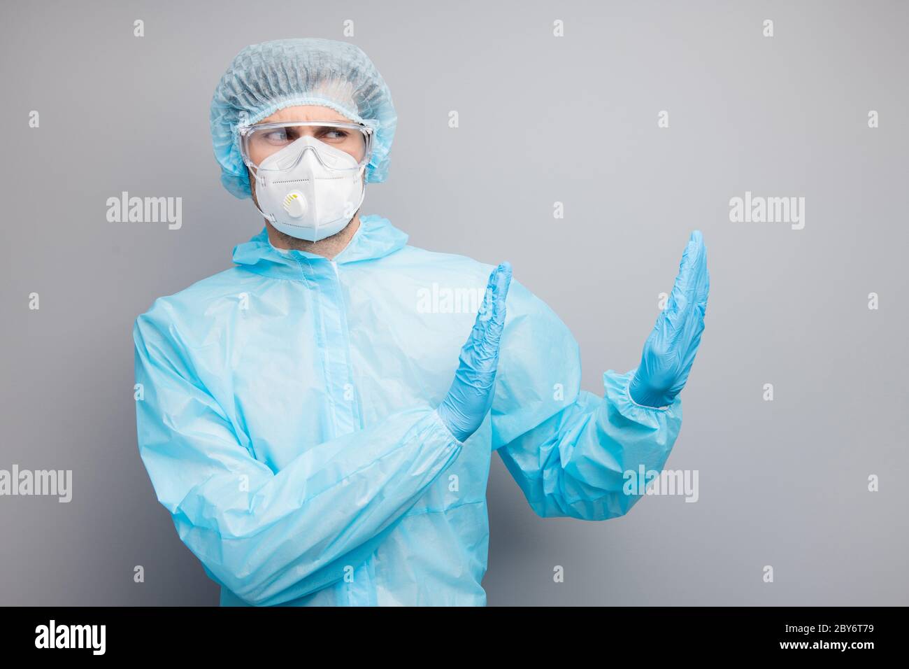 Photo of expert doc virologist guy raise palms side empty space stop patients danger infected zone wear gloves mask hazmat blue uniform surgical cap Stock Photo