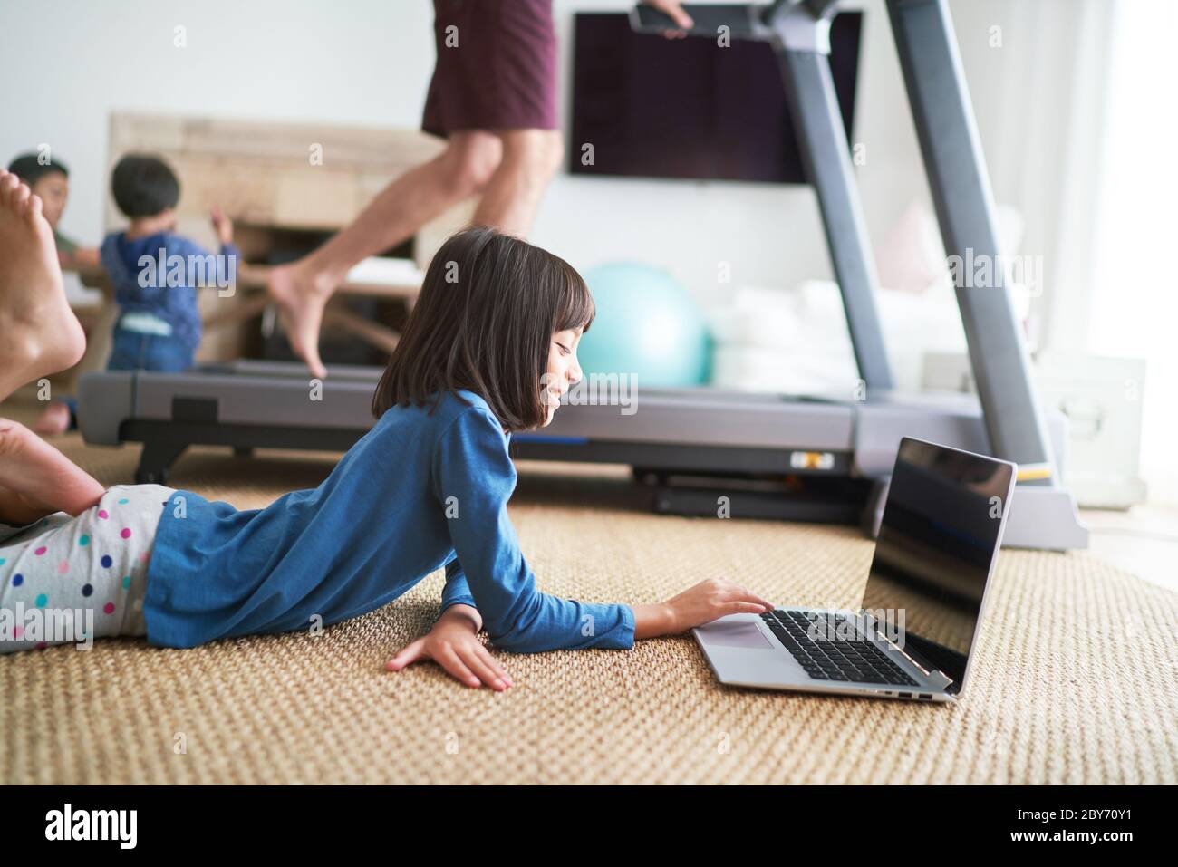 Girl using laptop on floor next to father on treadmill Stock Photo