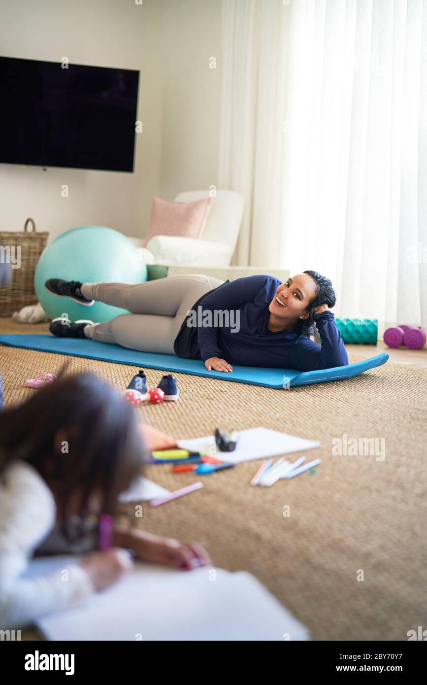 Smiling mother exercising while daughter draws in living room Stock Photo
