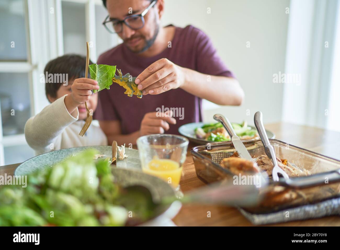 Playful father and son eating with toy dinosaur Stock Photo