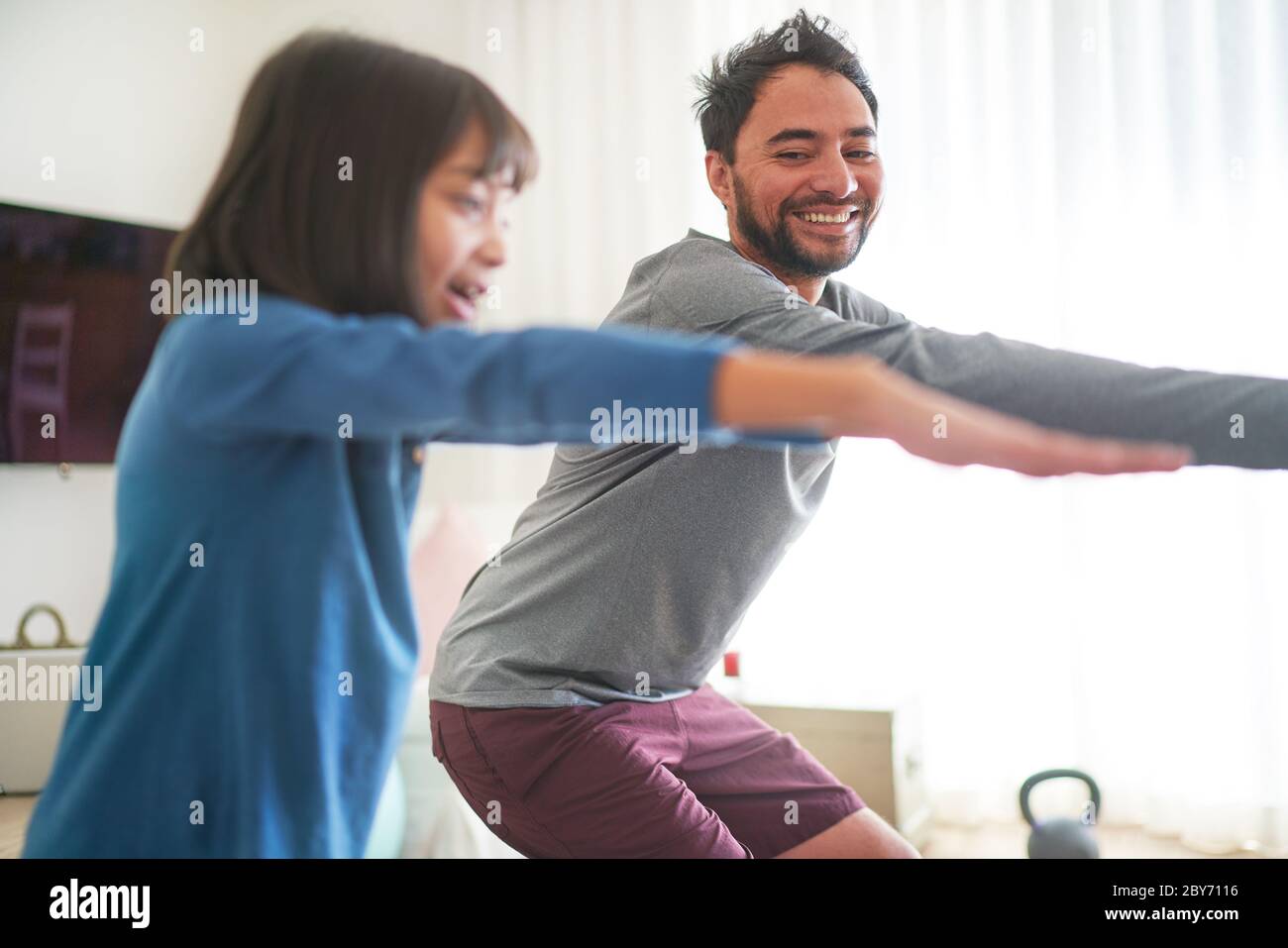 Happy father and daughter exercising in living room Stock Photo
