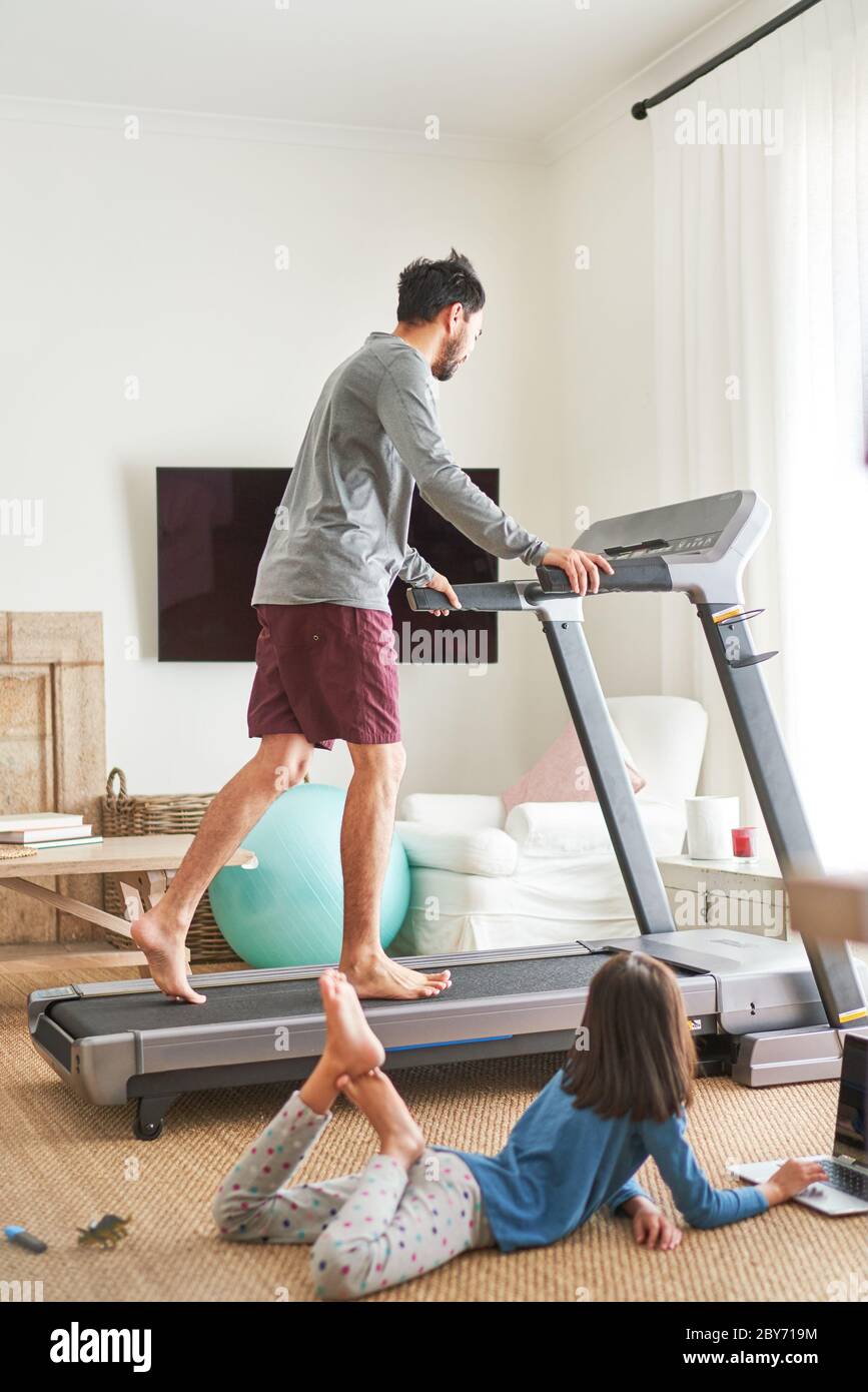 Daughter using laptop next to father on treadmill Stock Photo