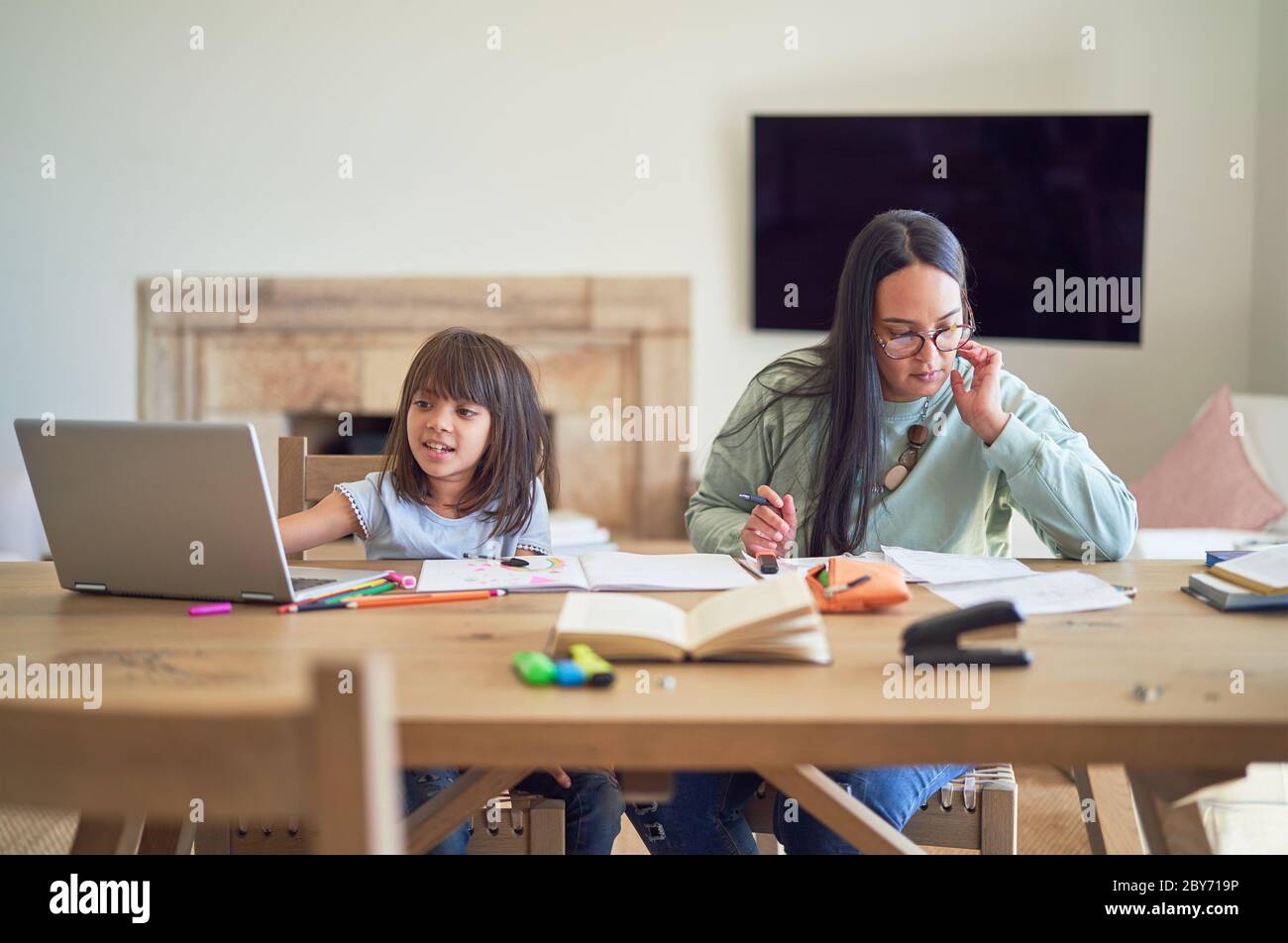Mother paying bills next to daughter homeschooling at table Stock Photo