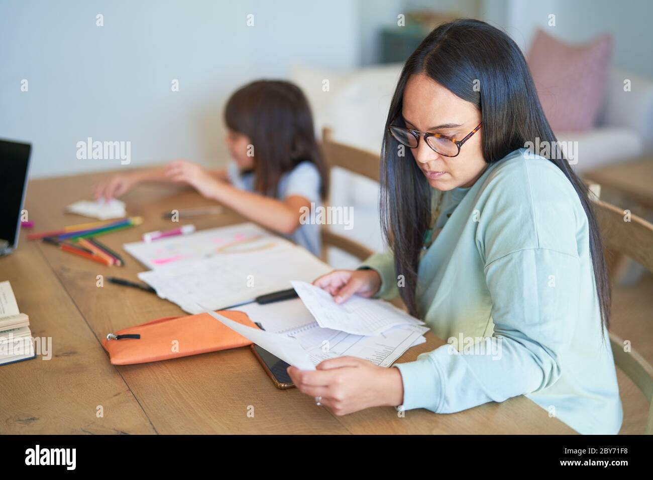 Woman paying bills next to daughter coloring at table Stock Photo