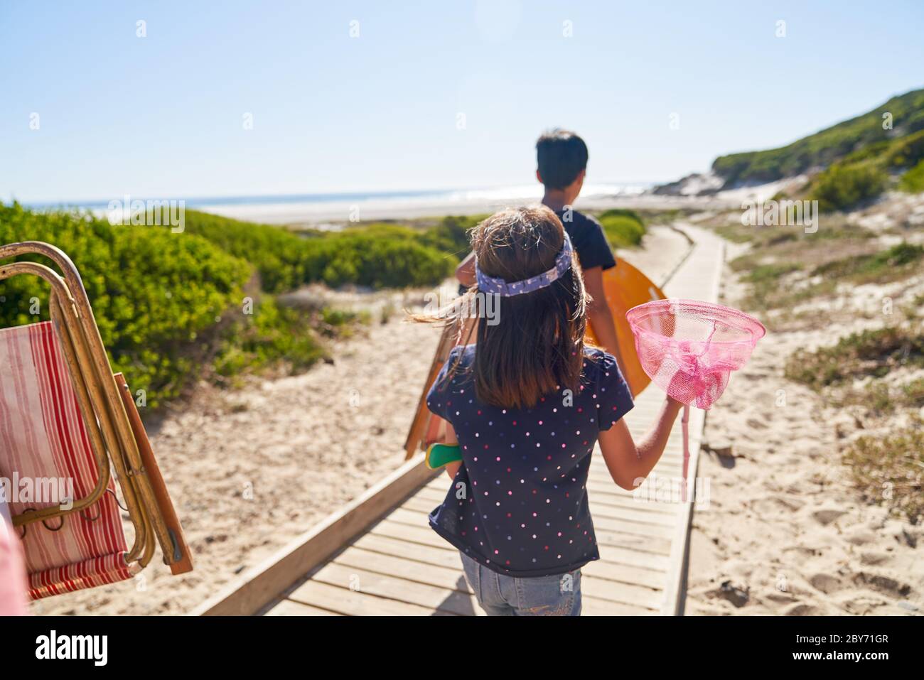 Girl carrying butterfly net on sunny beach boardwalk Stock Photo