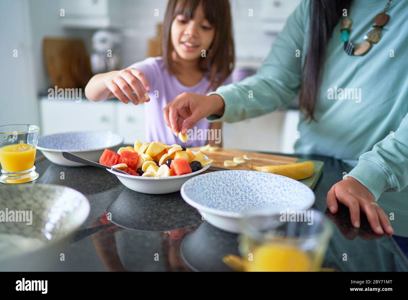 Mother and daughter eating fruit in kitchen Stock Photo