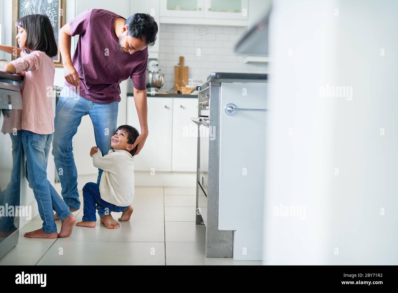 Affectionate boy hugging leg of father in kitchen Stock Photo