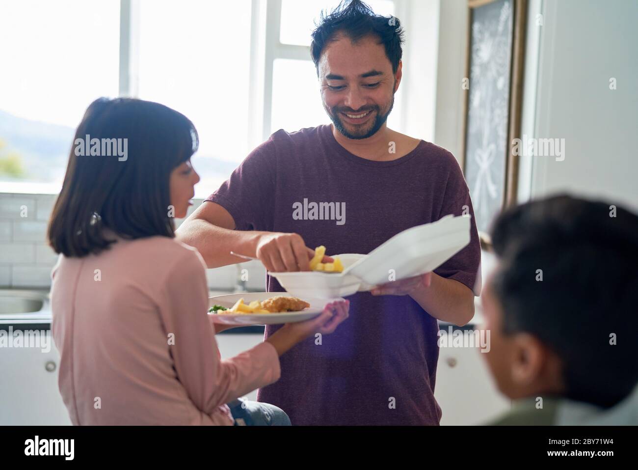 Happy father feeding daughter takeout food in kitchen Stock Photo