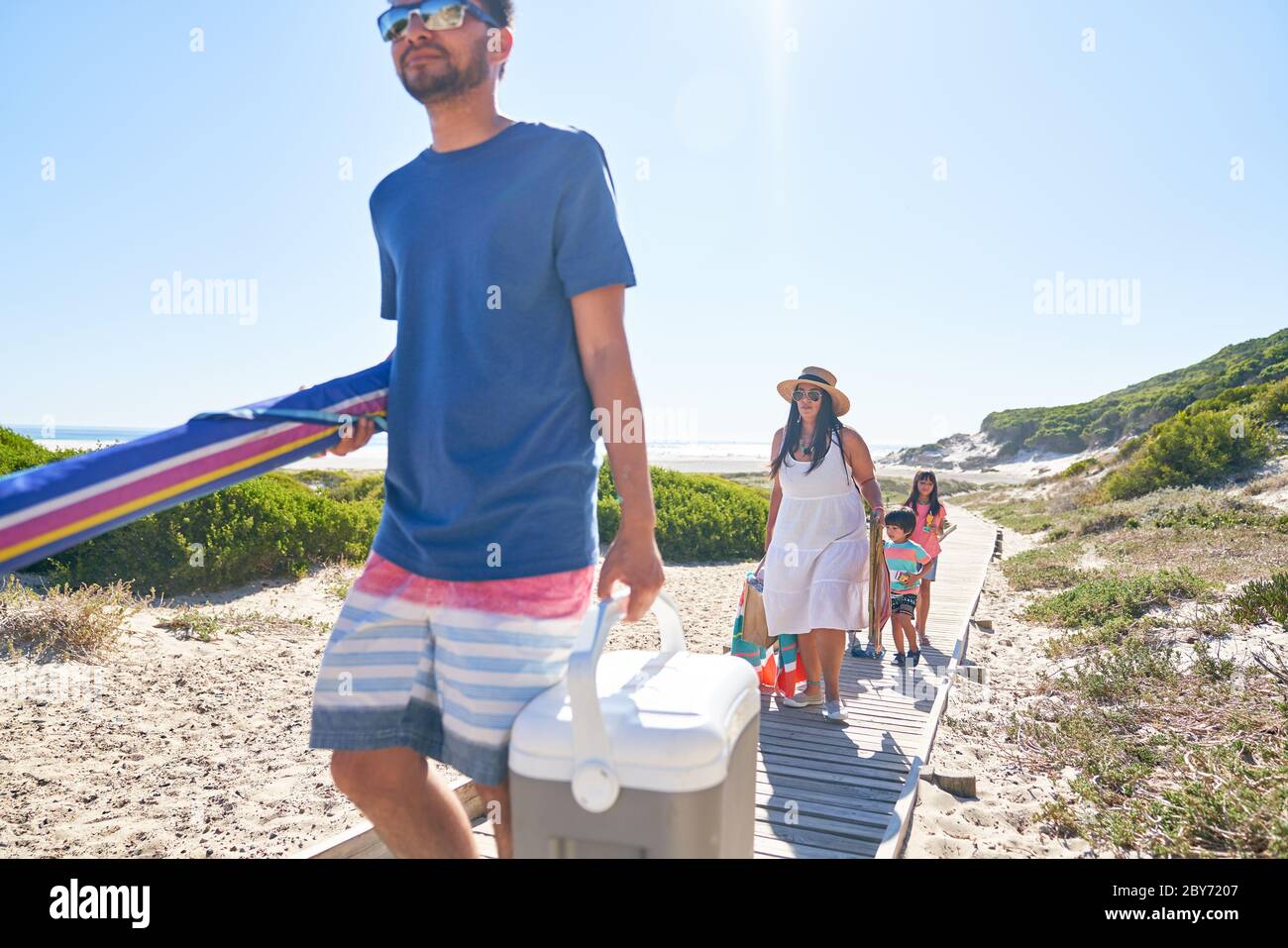 Family carrying beach equipment on sunny boardwalk Stock Photo