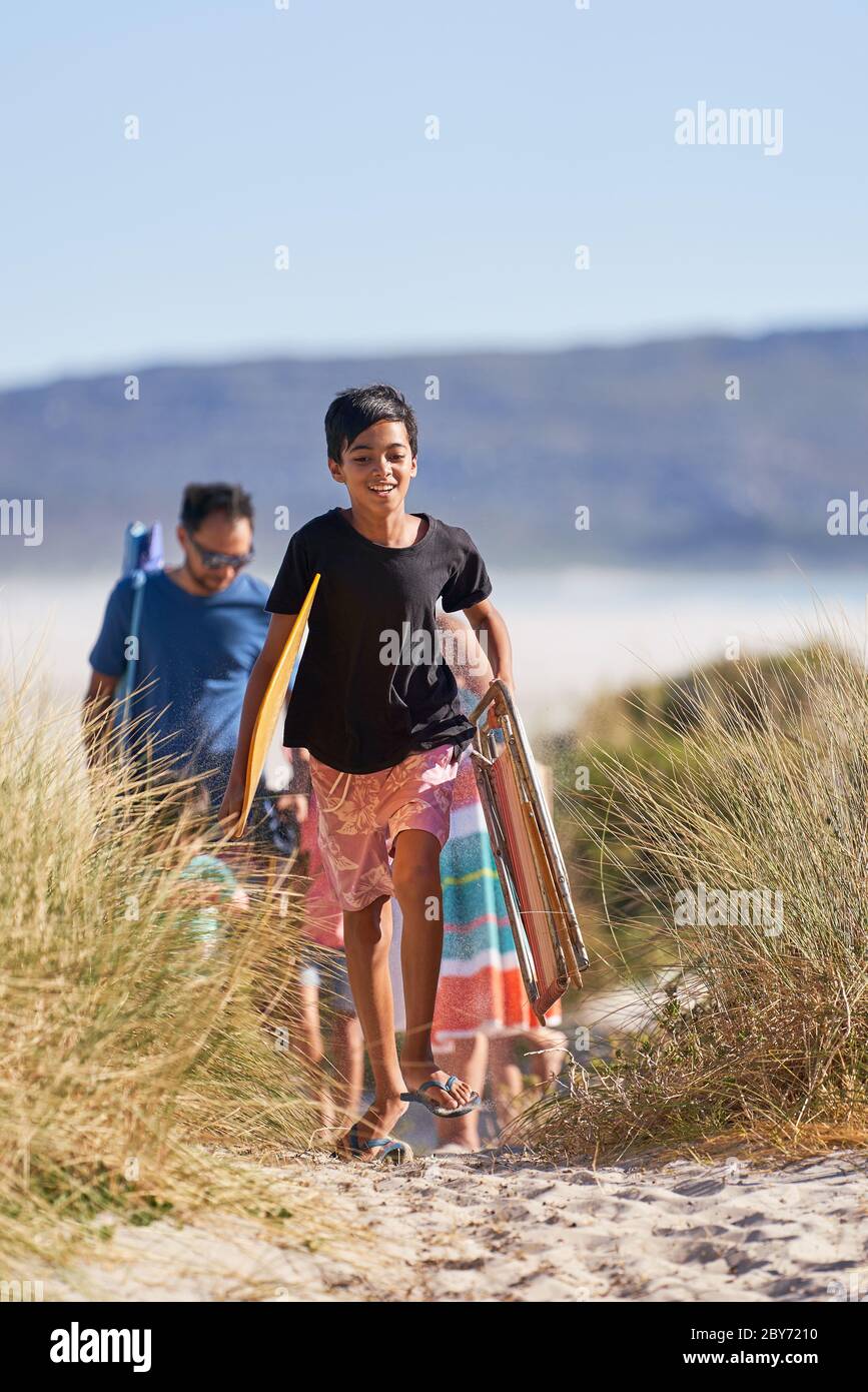 Happy boy carrying folding chair and towel on sunny beach Stock Photo