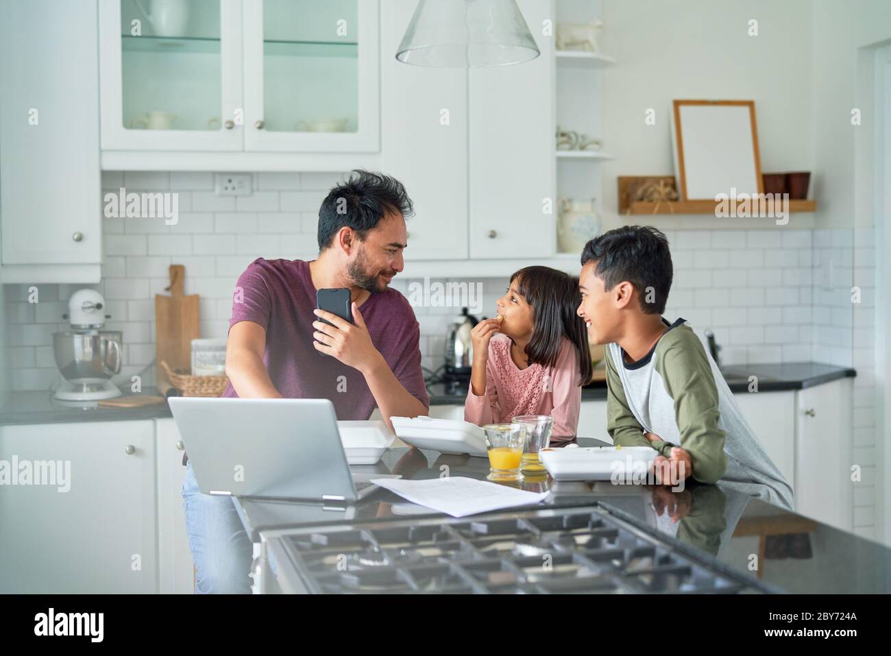 Father working in kitchen with kids eating takeout food Stock Photo