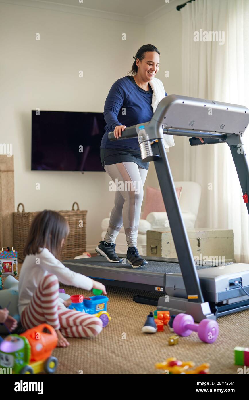Mother exercising on treadmill while daughter plays on floor Stock Photo