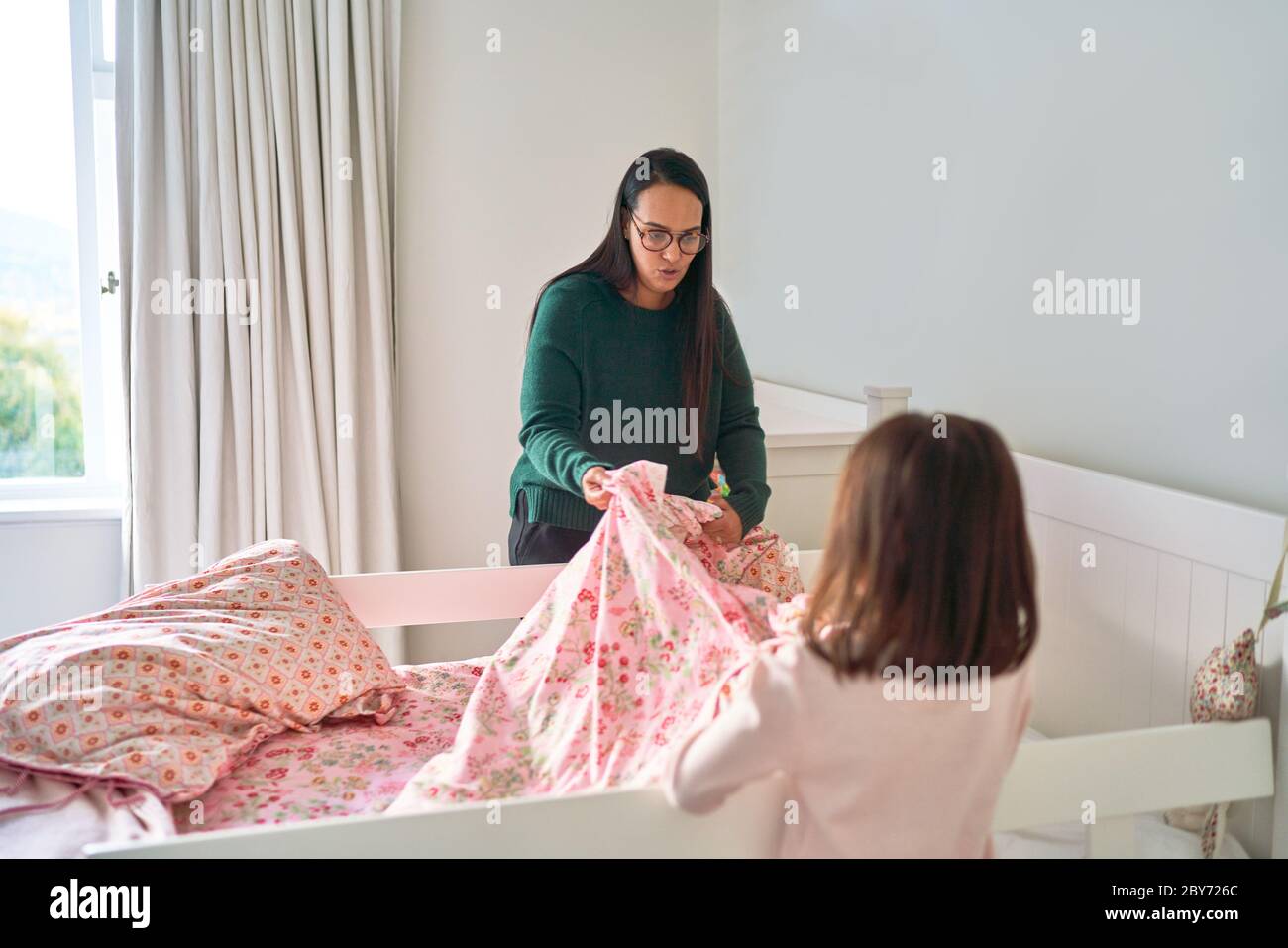 Mother helping daughter make bed Stock Photo