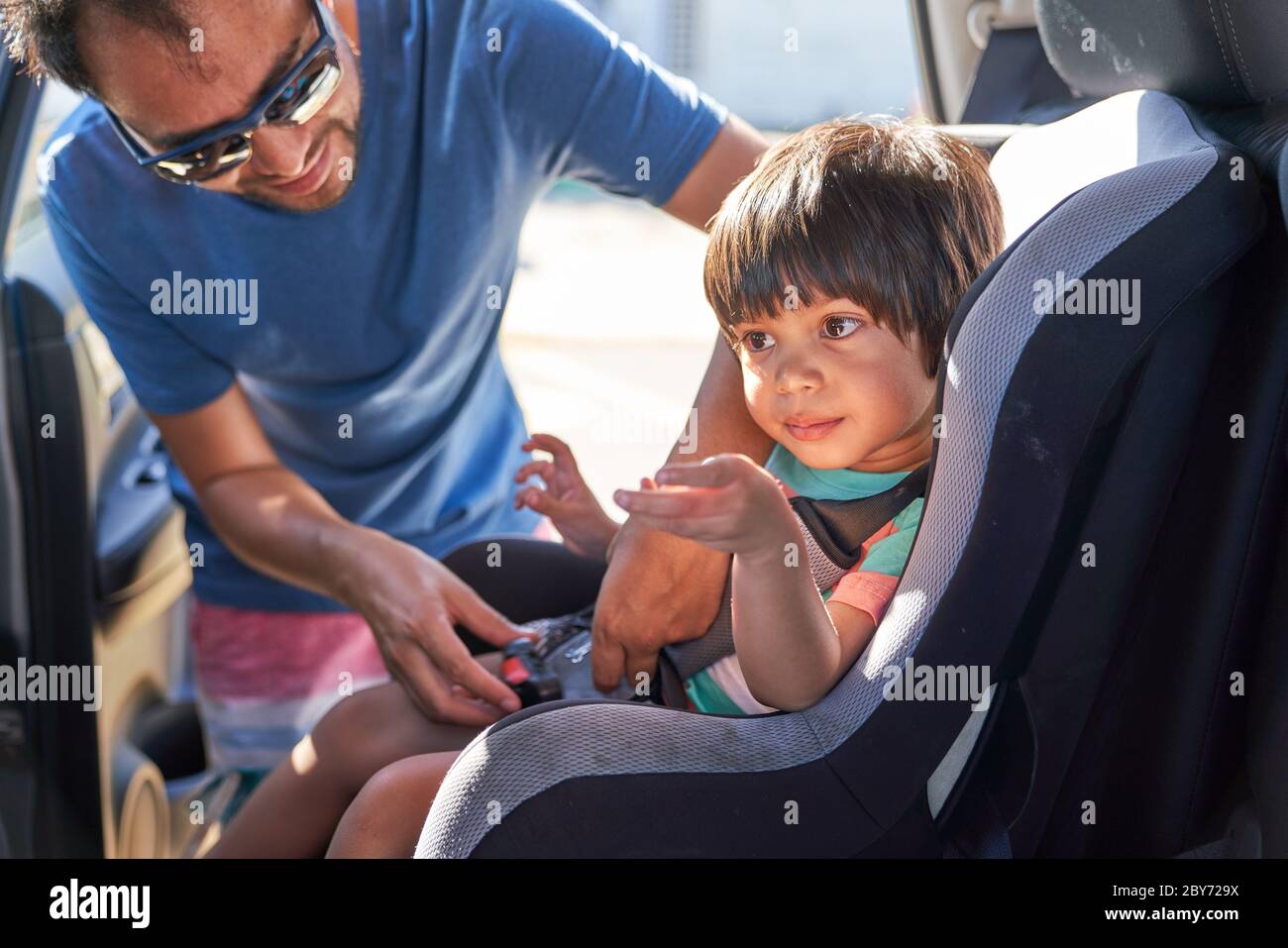 Father fastening son in car seat Stock Photo