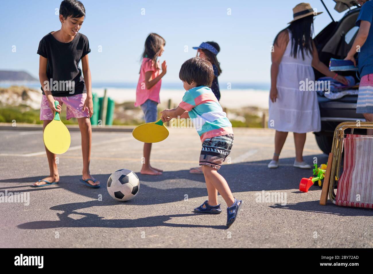 Family playing with soccer ball in beach parking lot Stock Photo
