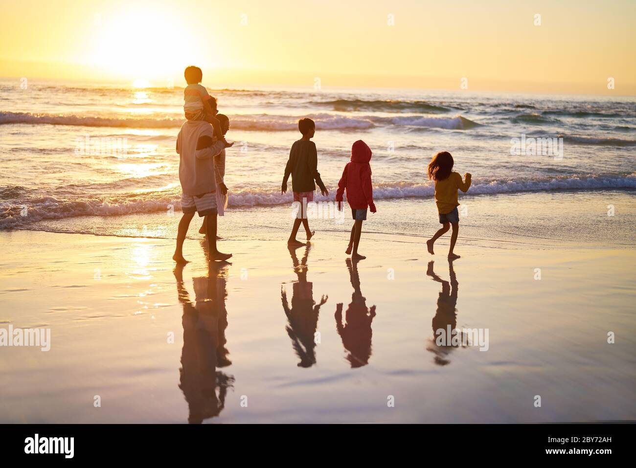 Family walking in ocean surf on beach at sunset Stock Photo