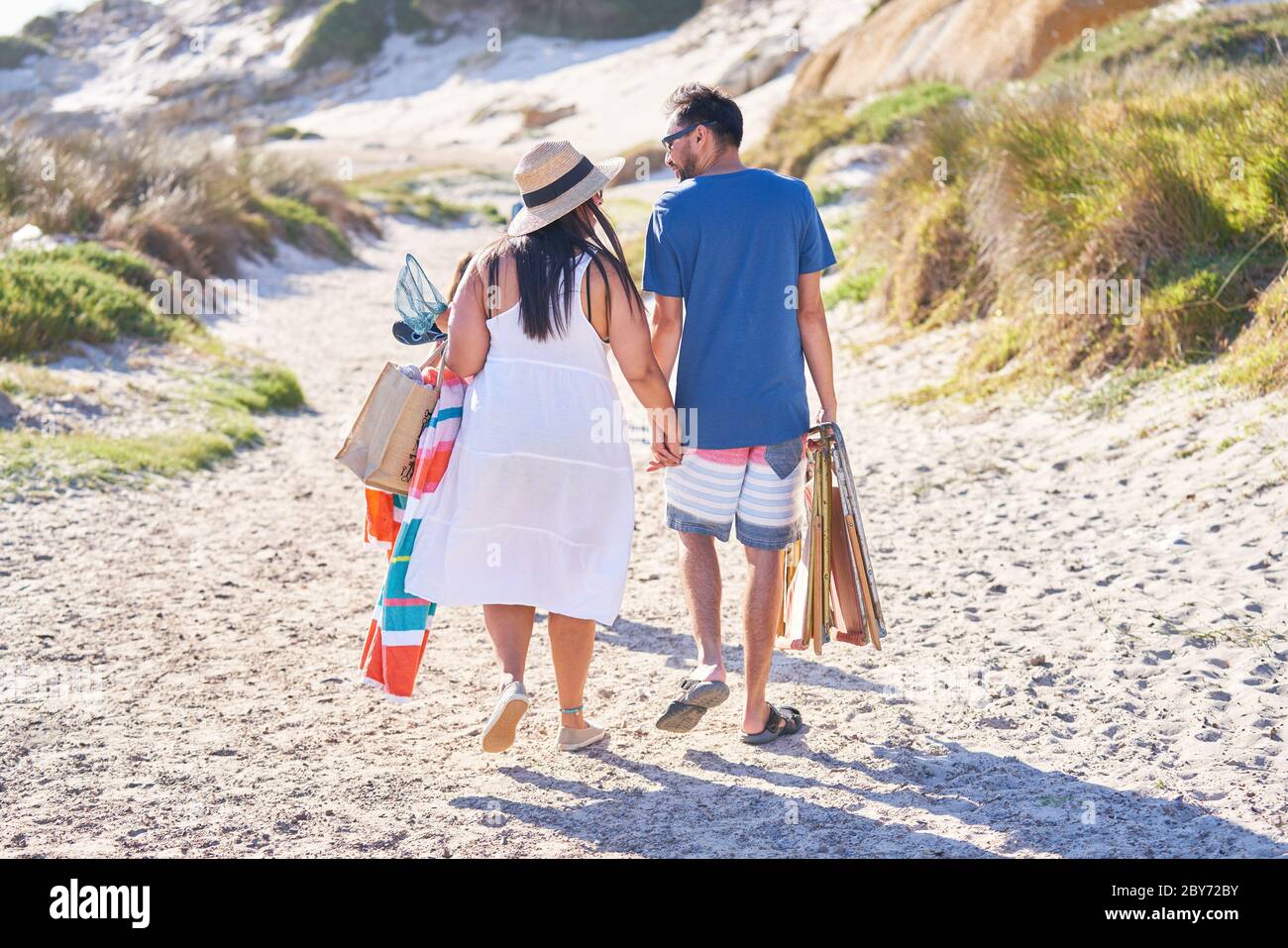 Affectionate couple walking on sunny beach path Stock Photo