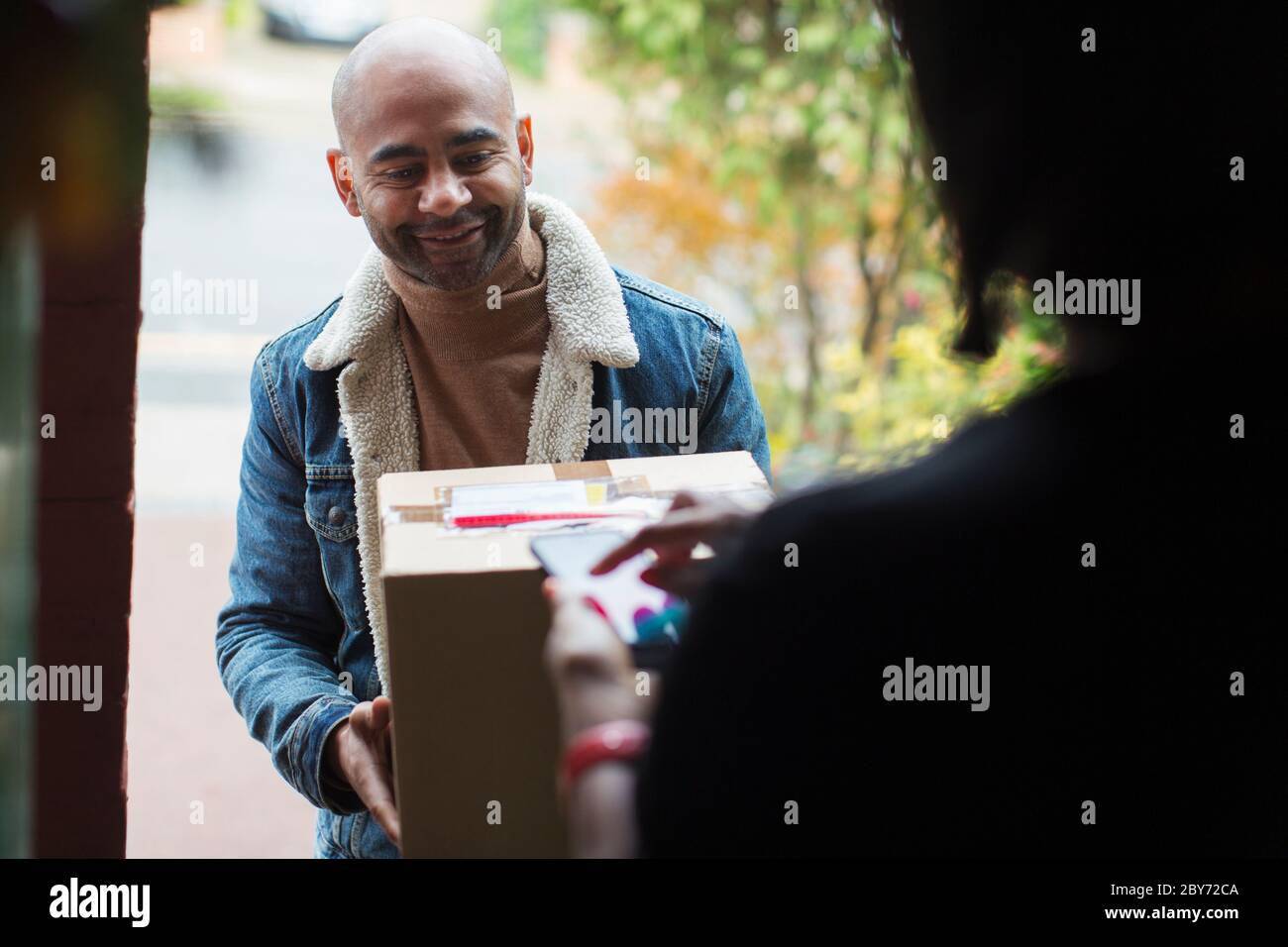 Delivery man delivering package to woman at front door Stock Photo