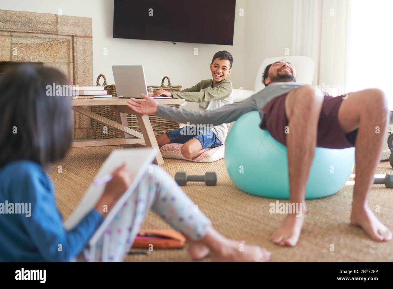 Happy father and kids exercising and doing homework in living room Stock Photo