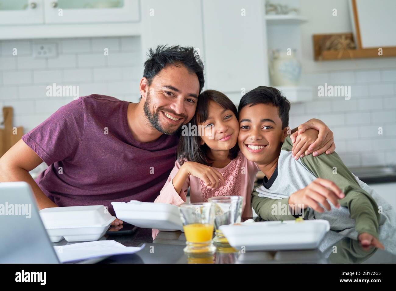 Portrait happy father and kids eating takeout food in kitchen Stock Photo