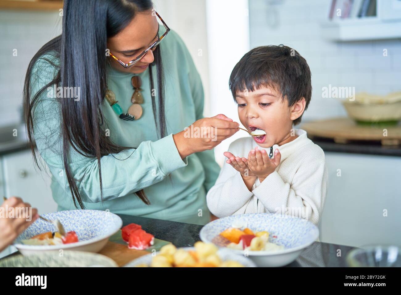 Mother feeding son in kitchen Stock Photo