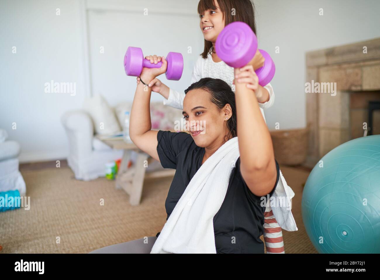 Daughter helping mother exercise with dumbbells in living room Stock Photo