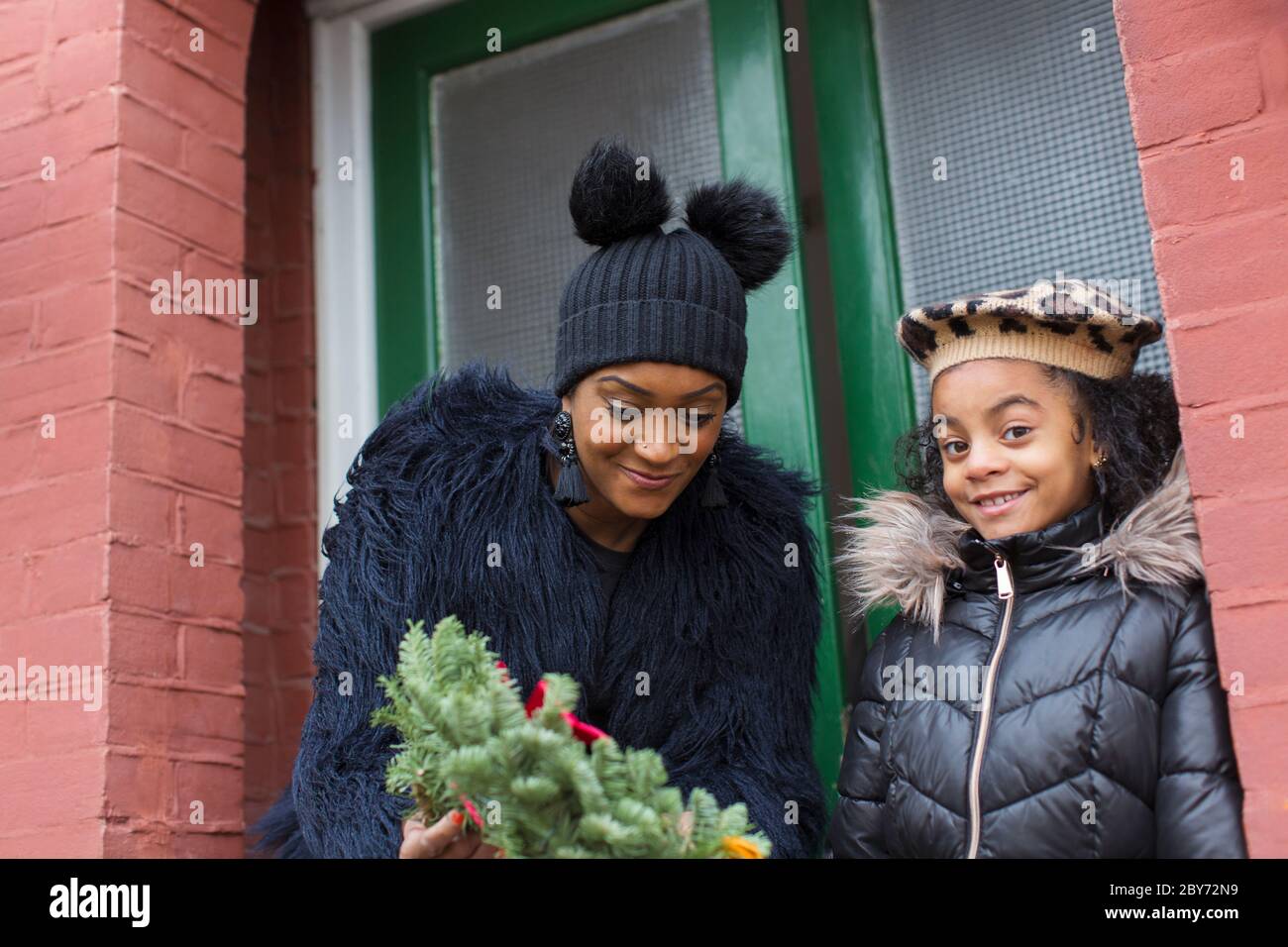 Happy mother and daughter with Christmas wreath on front stoop Stock Photo
