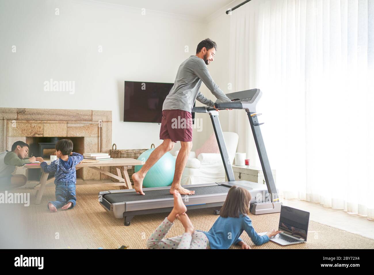 Father exercising on treadmill in living room with kids Stock Photo