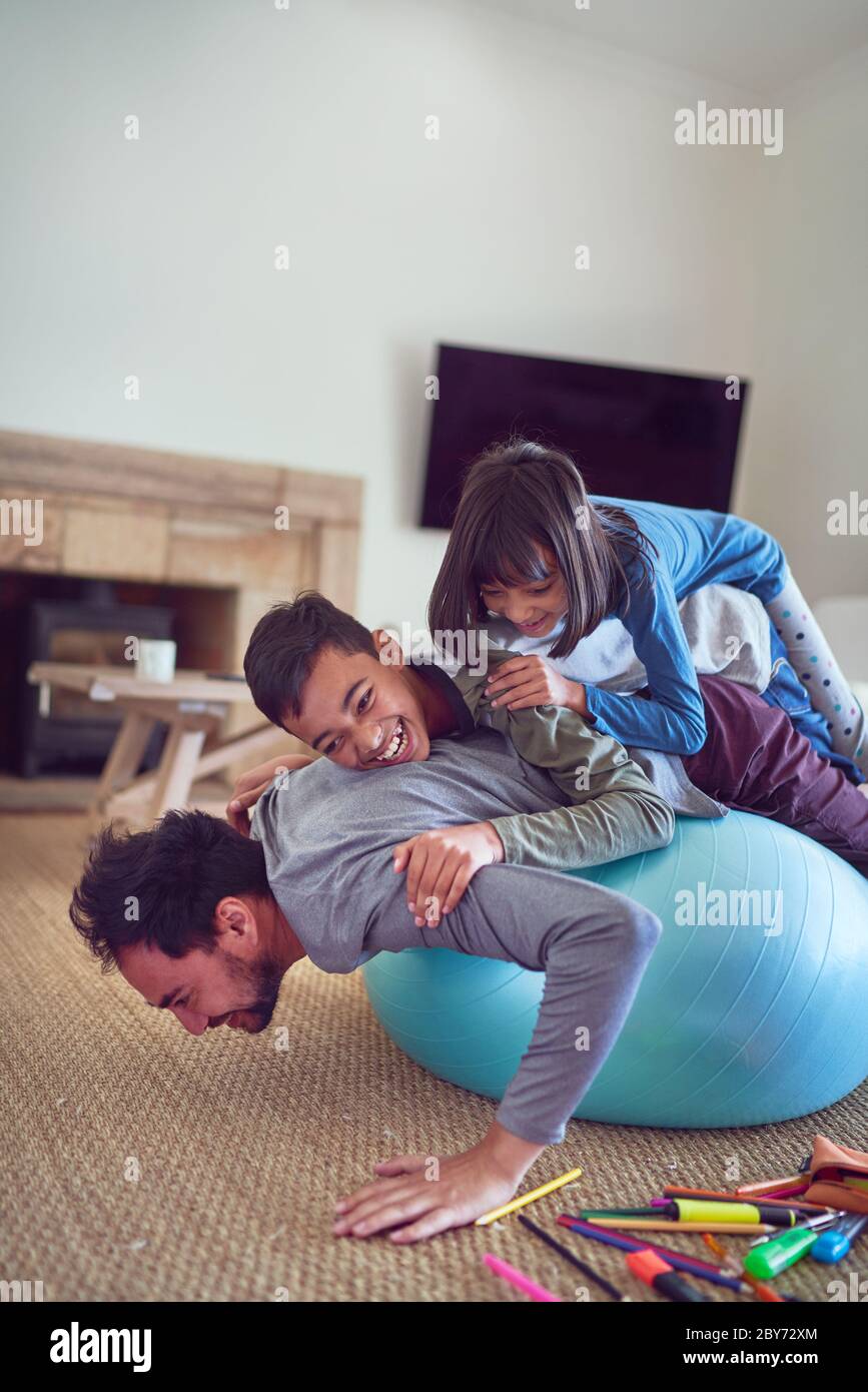 Playful kids on top of father exercising on fitness ball Stock Photo