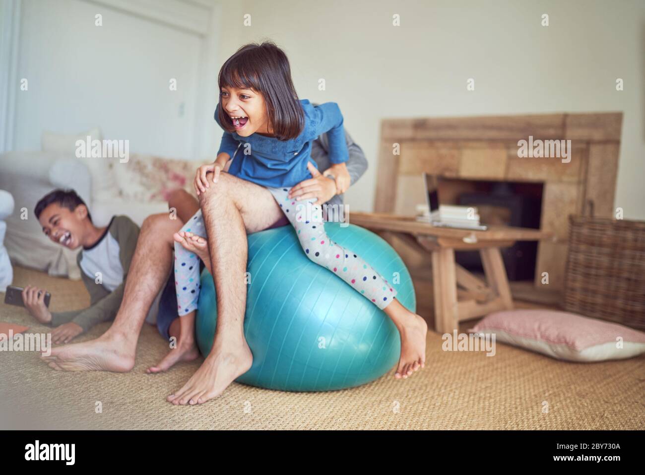 Happy family playing on fitness ball in living room Stock Photo